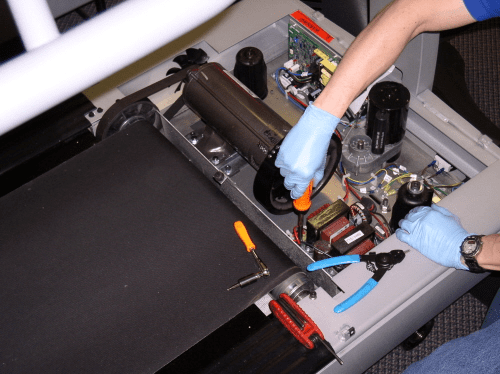 Technician repairing a treadmill motor with tools and gloves on.
