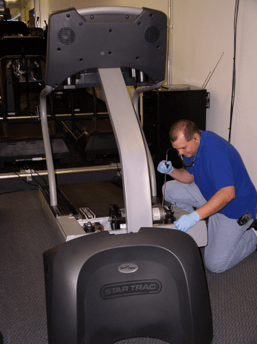 Technician repairing a Star Trac treadmill in a gym.