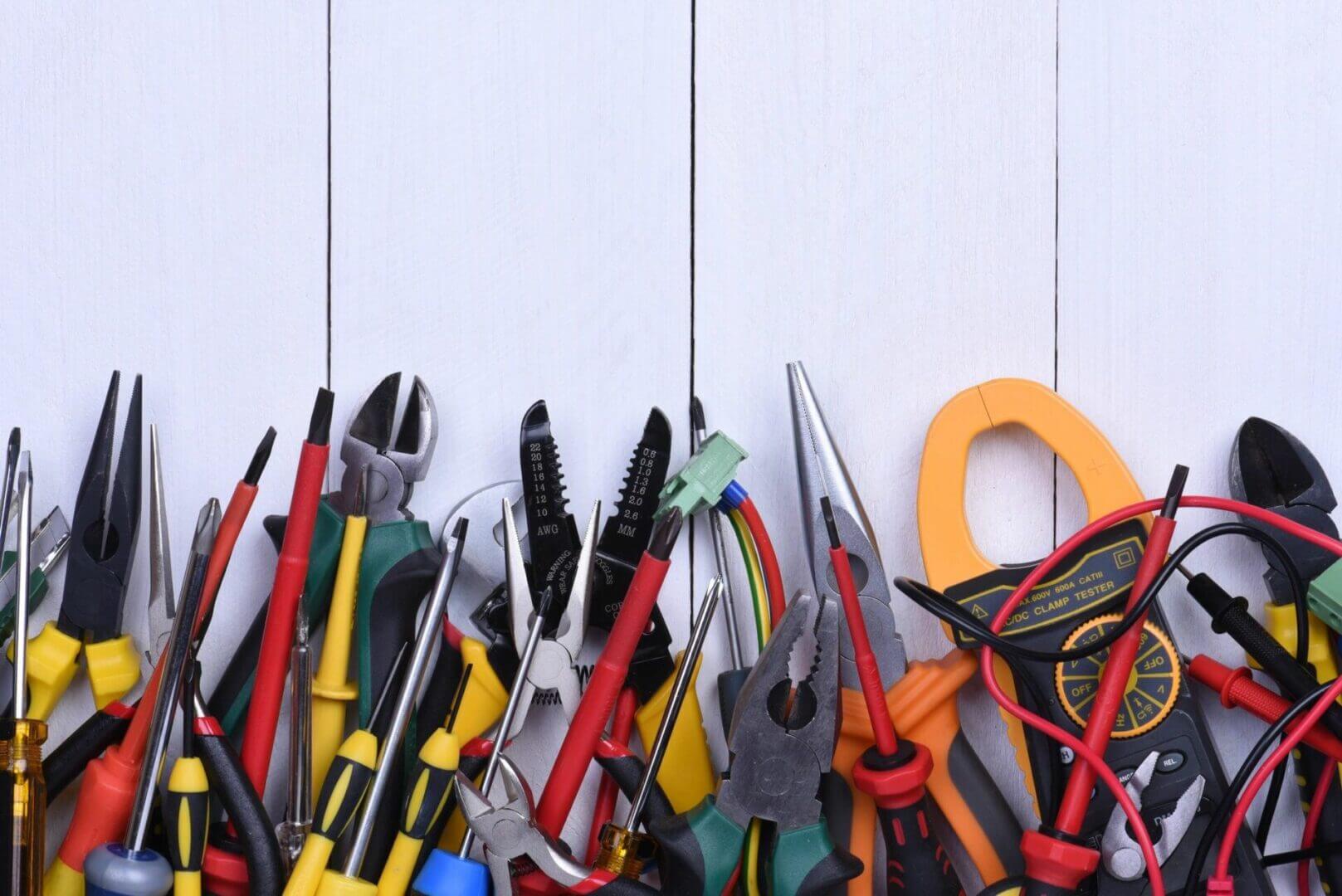 A collection of various hand tools and electrical testing equipment arranged on a white wooden surface.