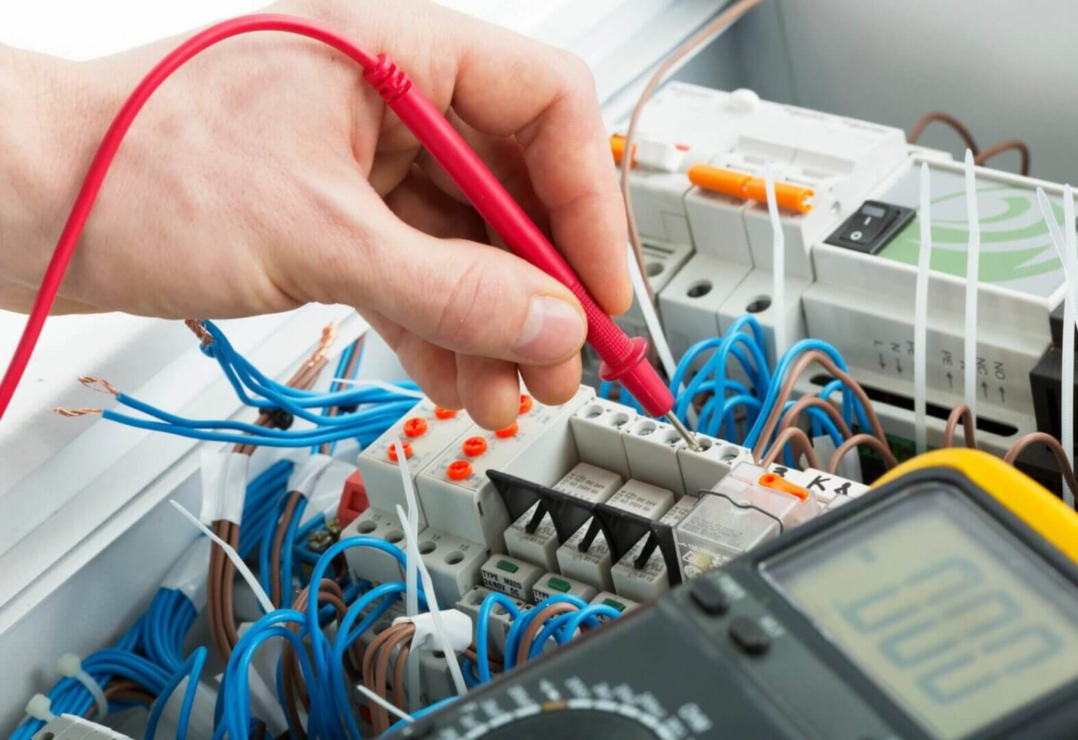Hand testing electrical circuit with red probe and multimeter.