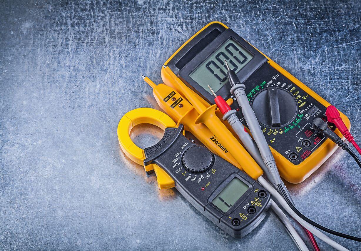 Digital multimeter and clamp meter tools on a scratched metal surface.