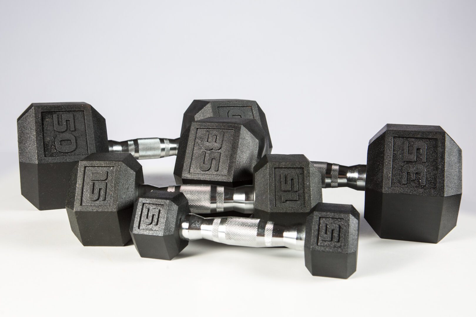 Set of black hexagonal dumbbells with silver handles on a white surface.